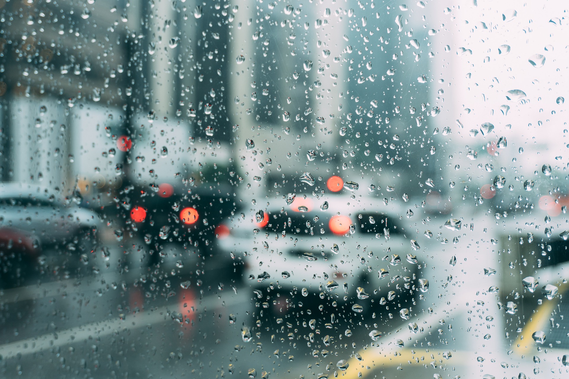 Cuidados a ter com a chuva quando conduzir. Uma estrada com veículos através duma janela molhada